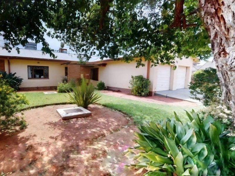 Front view of a single-story residential property featuring a double garage, metal roofing, and established garden area.