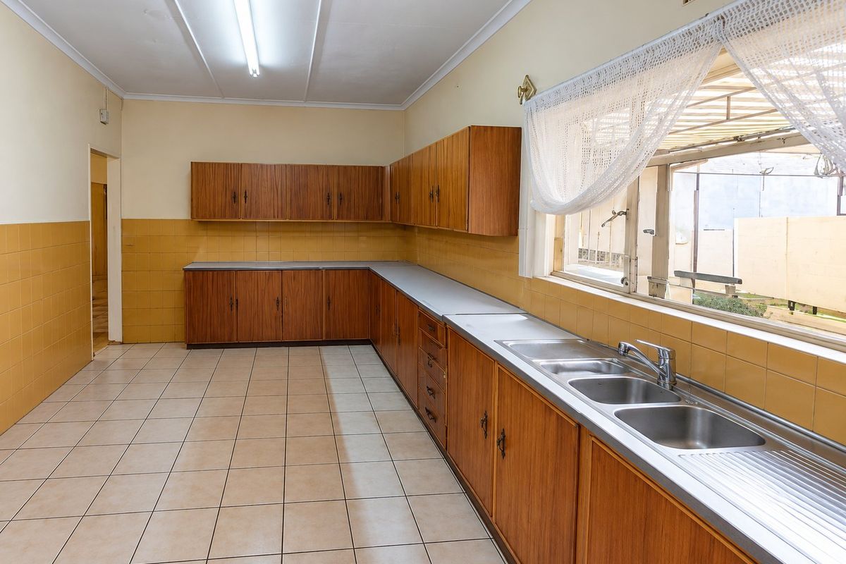 A spacious, empty kitchen featuring original wood-look cabinetry, double stainless steel sink, and tiled surfaces, offering a blank canvas for modern renovation.