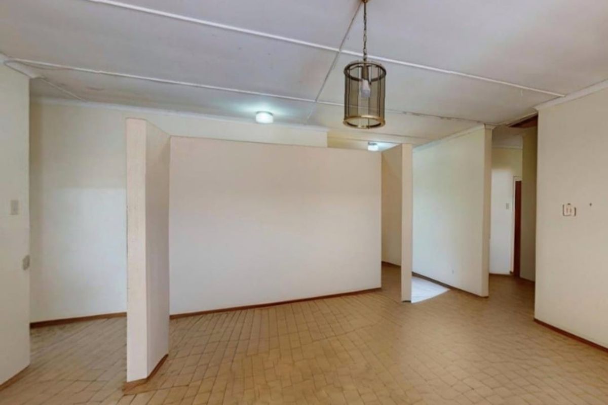 An empty living area featuring tiled flooring, a central pendant light, and a partition wall, requiring cosmetic updates to the ceiling and flooring.