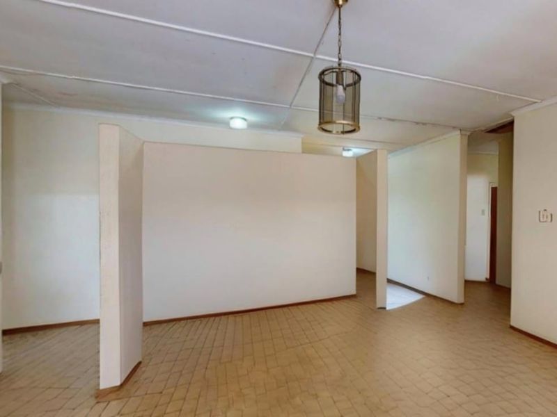 An empty living area featuring tiled flooring, a central pendant light, and a partition wall, requiring cosmetic updates to the ceiling and flooring.