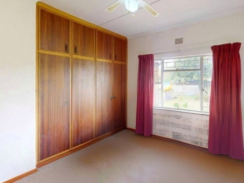 A vacant bedroom featuring built-in wooden cupboards, a ceiling fan, and a metal-framed window with views of the garden.