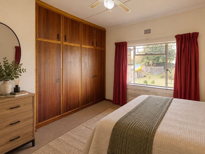 A bedroom featuring a large built-in wooden wardrobe, ceiling fan, and a window overlooking the rear garden.