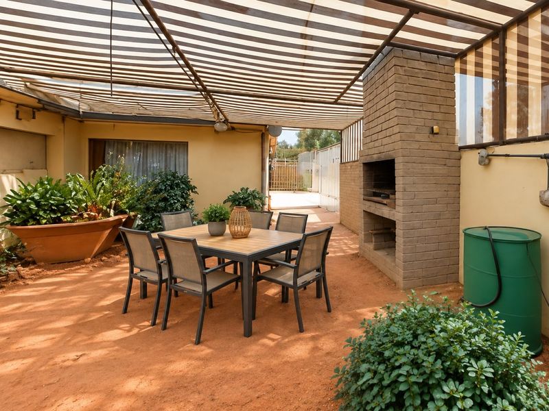 A covered outdoor patio area featuring a built-in brick braai and a striped overhead canopy, providing a functional space for outdoor entertaining.