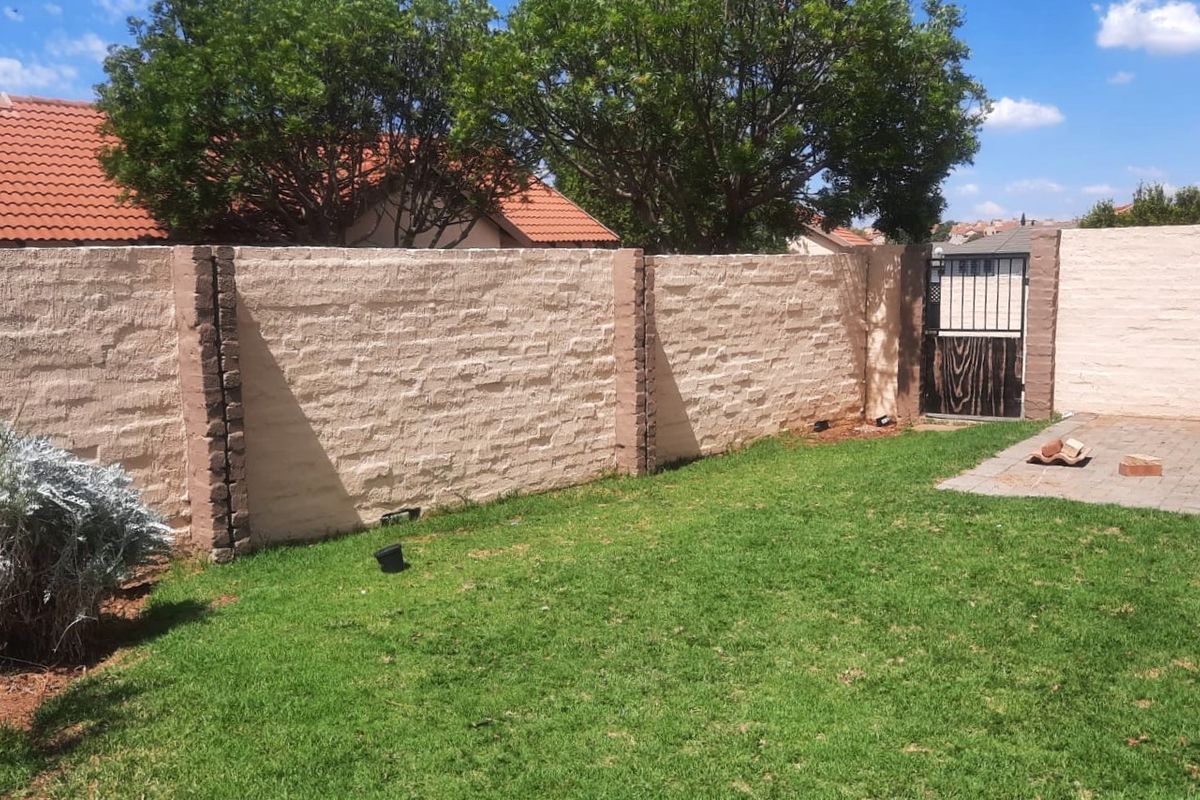 A private rear garden featuring a textured perimeter wall, a small paved section, and a metal access gate.