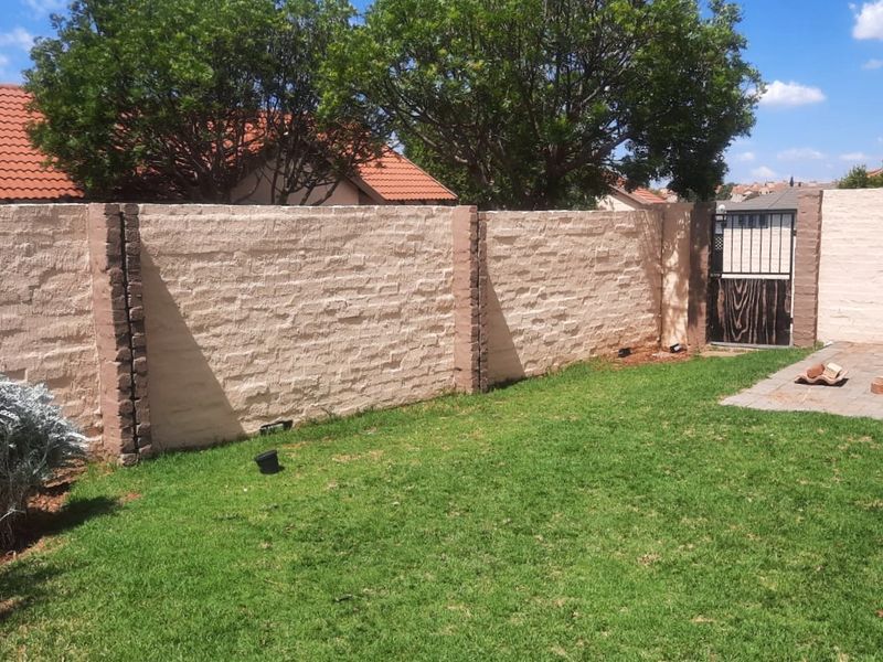 A private rear garden featuring a textured perimeter wall, a small paved section, and a metal access gate.