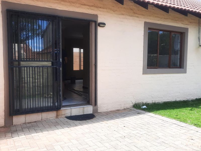 Rear exterior view of the apartment featuring a paved patio area, security gate, and satellite dish installation.