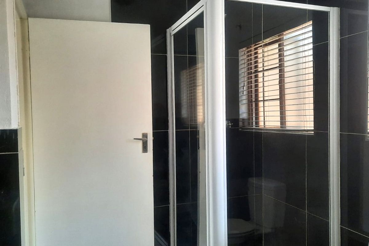A bathroom featuring a shower enclosure, toilet, and dark wall tiling with fitted venetian blinds.