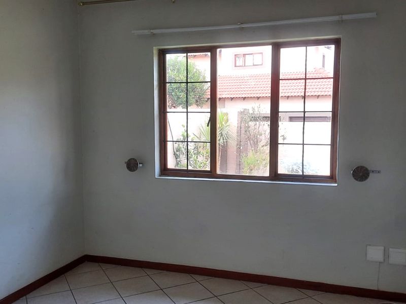 An empty bedroom featuring tiled flooring, wooden window frames, and neutral wall finishes, offering a blank canvas for personalization.