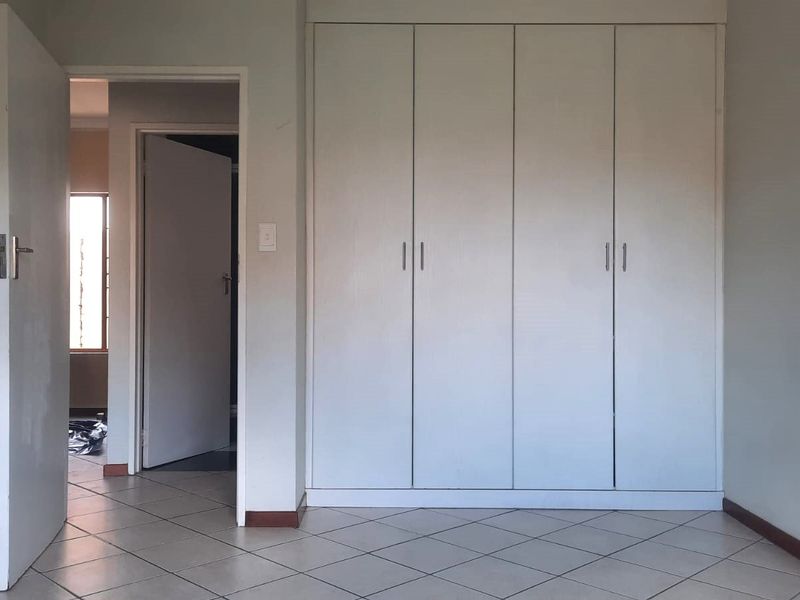 A clean, empty bedroom featuring neutral tiled flooring and white built-in cupboards, offering a blank canvas for personalization.