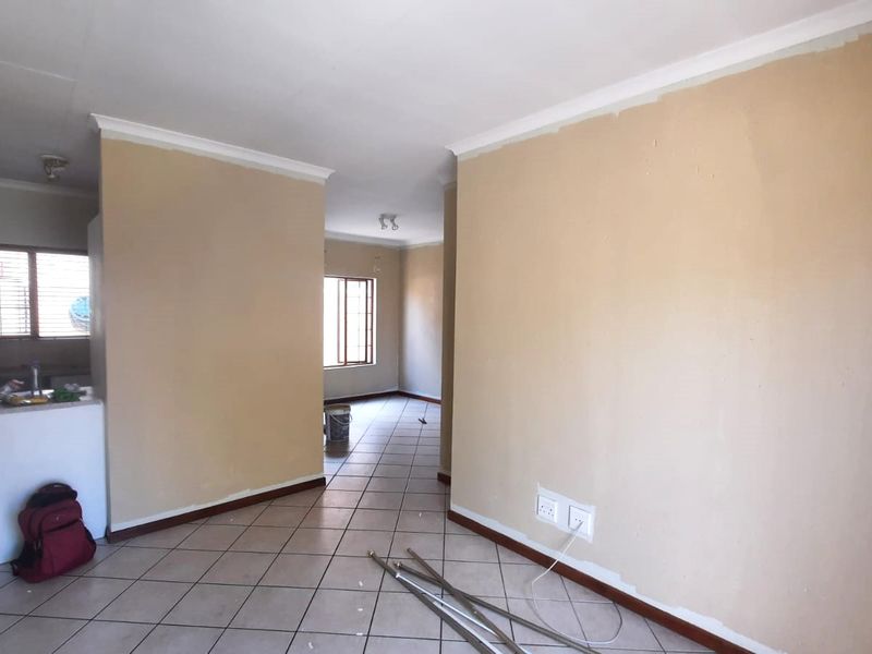 An open-plan living and kitchen area featuring tiled flooring and neutral wall tones, currently vacant and ready for renovation or staging.