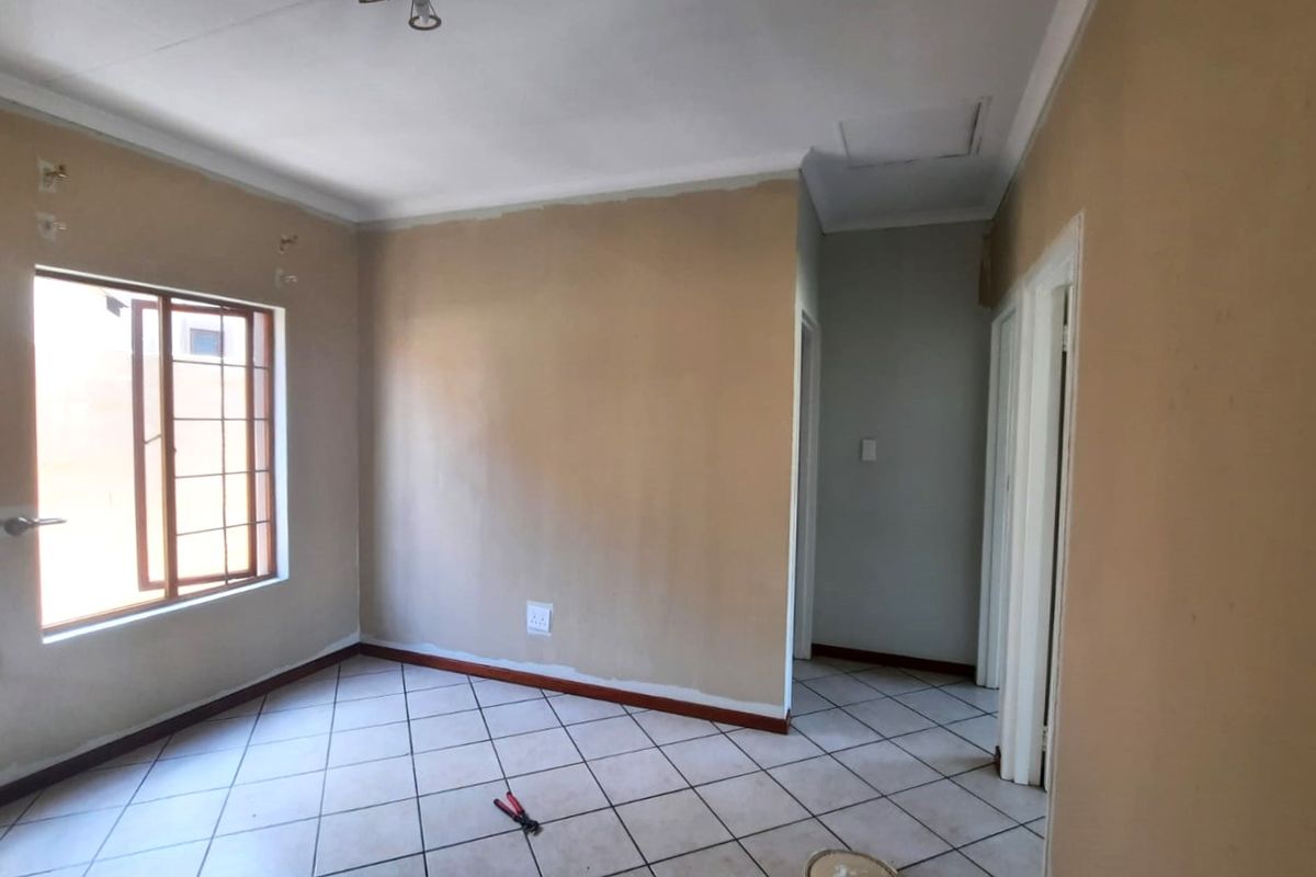 An empty bedroom featuring tiled flooring, a window with security bars, and neutral wall finishes requiring minor cosmetic touch-ups.