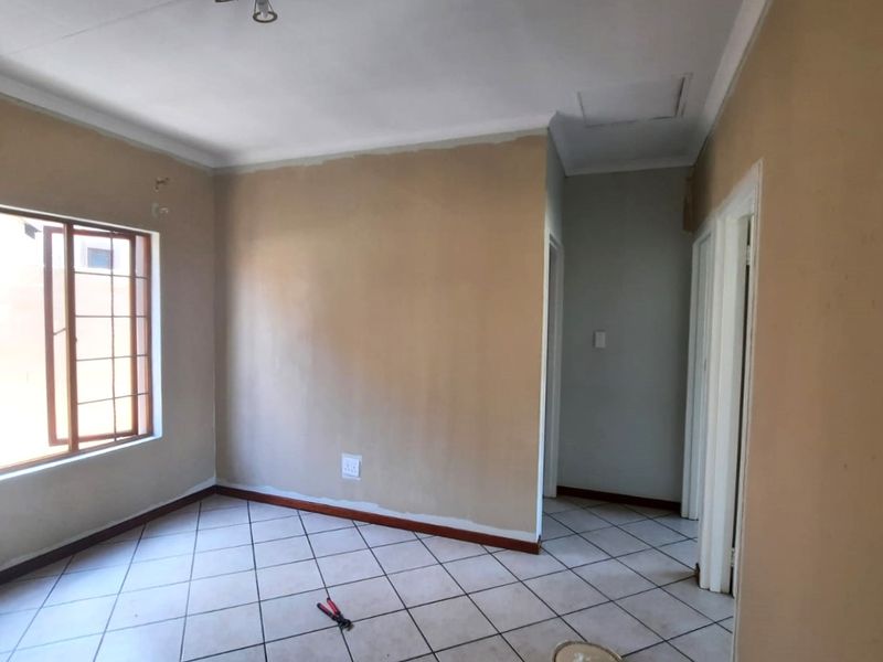 An empty bedroom featuring tiled flooring, a window with security bars, and neutral wall finishes requiring minor cosmetic touch-ups.
