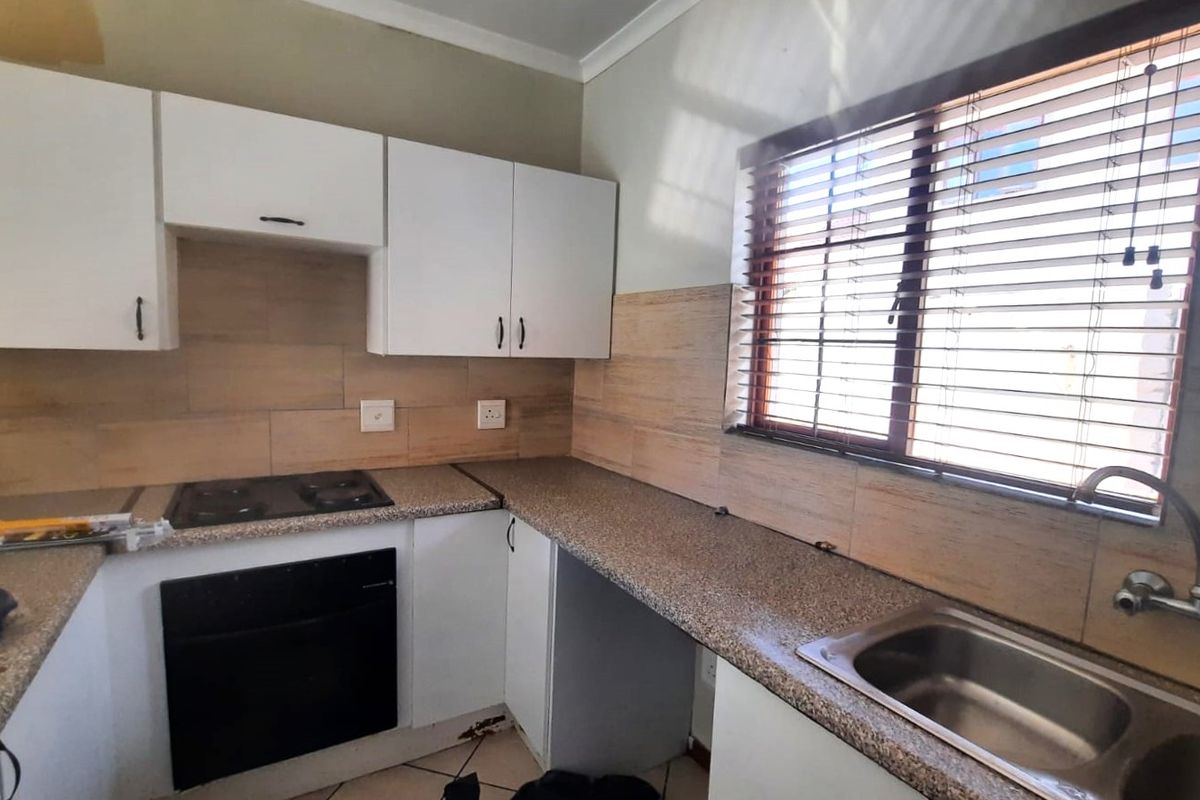 A functional kitchen featuring white cabinetry, granite countertops, a built-in oven and hob, and a stainless steel sink with a tiled backsplash.
