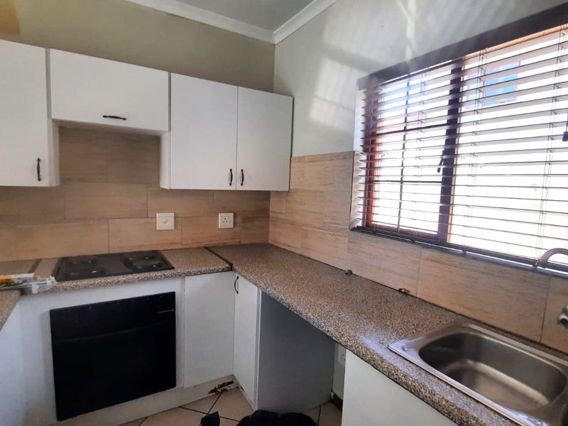 A functional kitchen featuring white cabinetry, granite countertops, a built-in oven and hob, and a stainless steel sink with a tiled backsplash.