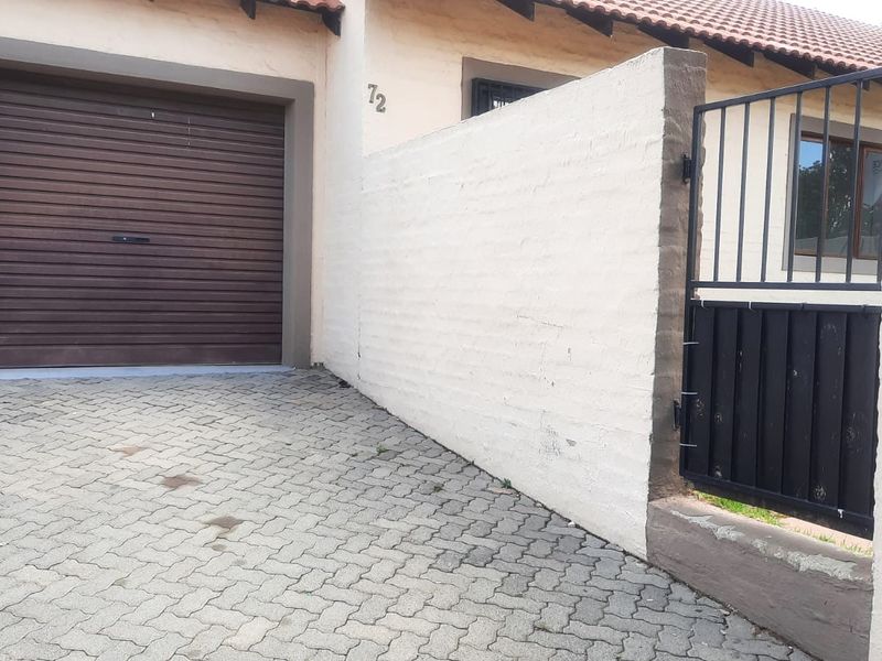 Front exterior view of the apartment featuring a paved driveway, a secure roller garage door, and a gated pedestrian entrance.