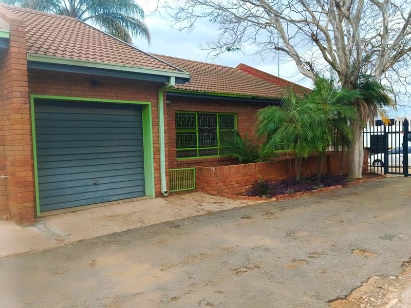 Front elevation of a brick townhouse featuring a single garage, tiled roof, and security-fitted windows with established garden landscaping.