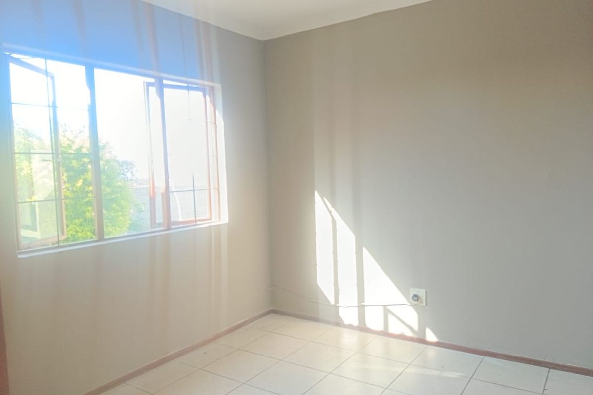 A bright, empty bedroom featuring neutral wall paint, tiled flooring, and a large casement window allowing for natural light.