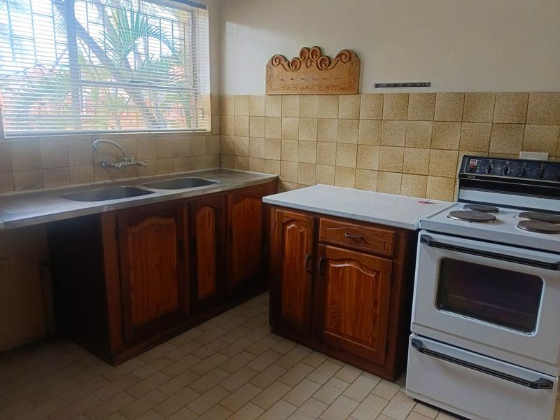 A functional kitchen featuring wooden cabinetry, a double basin sink, tiled backsplash, and a freestanding electric stove with a window view.