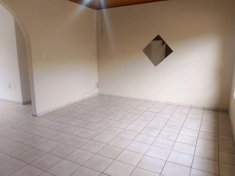 An empty living room featuring neutral tiled flooring, an arched entryway, and timber ceiling trim, providing a blank canvas for interior design.