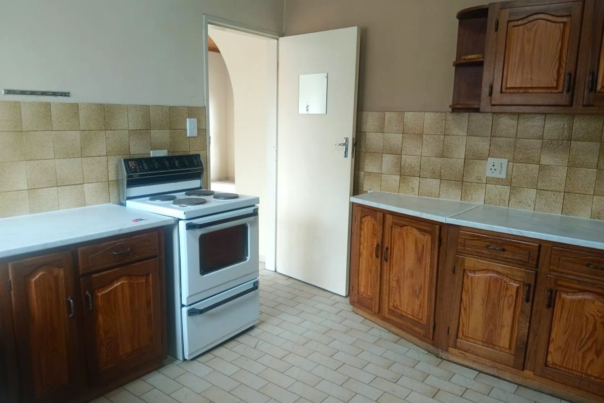 A functional kitchen featuring wooden cabinetry, tiled backsplash, and a freestanding electric stove, offering a dated aesthetic ready for modernization.