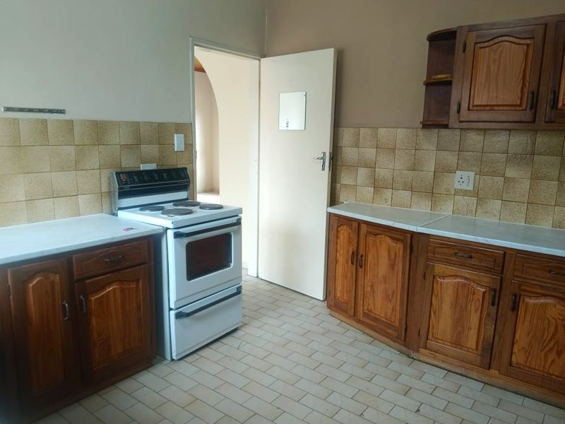 A functional kitchen featuring wooden cabinetry, tiled backsplash, and a freestanding electric stove, offering a dated aesthetic ready for modernization.