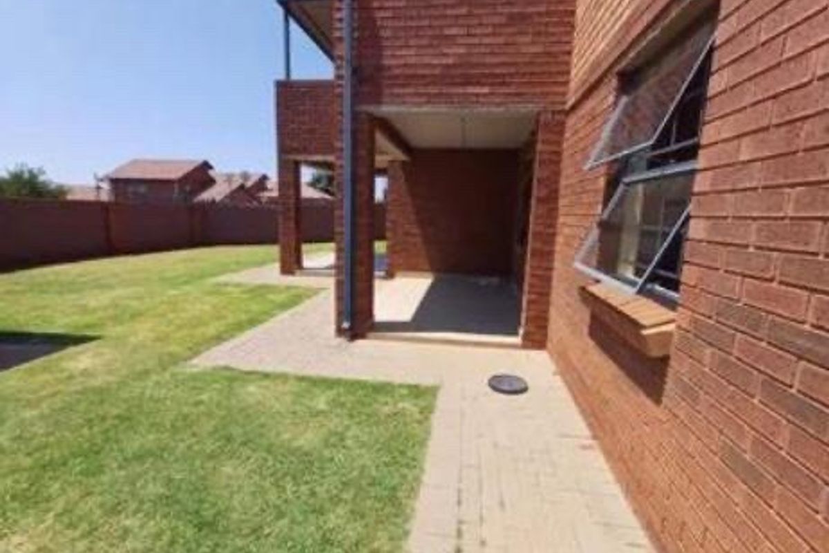 Rear view of the apartment building featuring a brick facade, a covered patio area, and a private lawn with boundary walling.