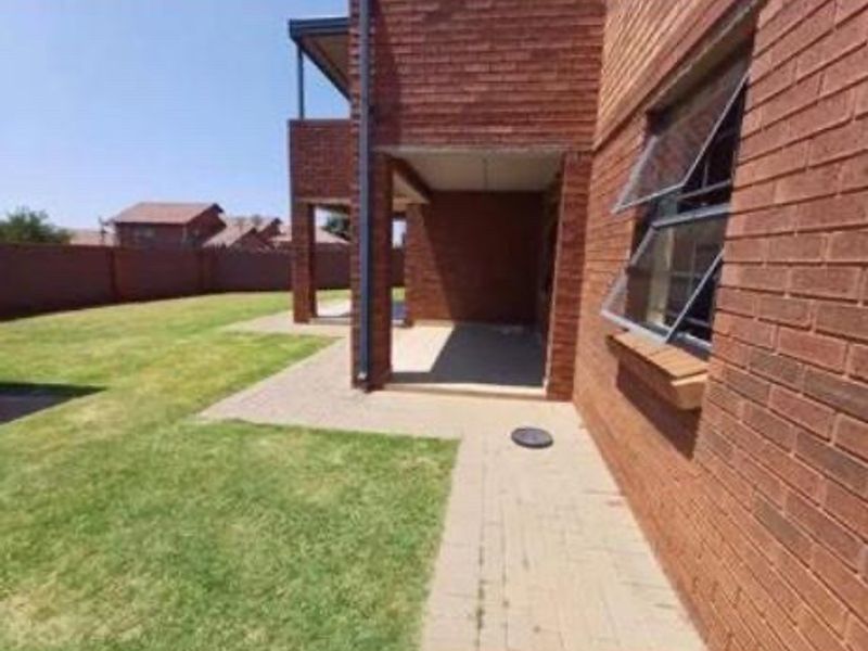 Rear view of the apartment building featuring a brick facade, a covered patio area, and a private lawn with boundary walling.