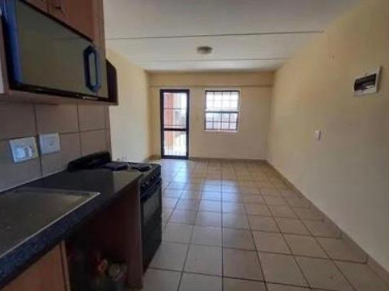 An empty open-plan kitchen and living area featuring tiled flooring, built-in cabinetry, and a security gate leading to the exterior.