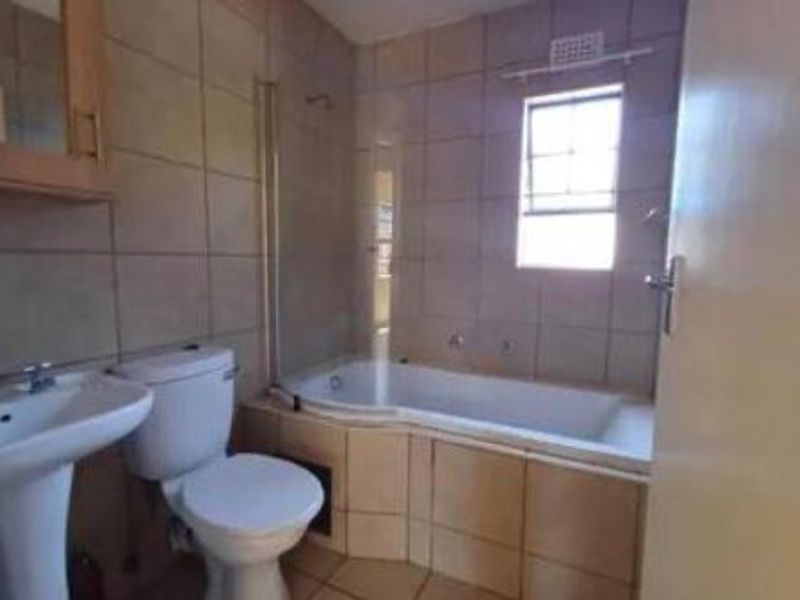 A functional bathroom featuring a pedestal basin, toilet, and a built-in bathtub with a glass shower screen and tiled finishes.