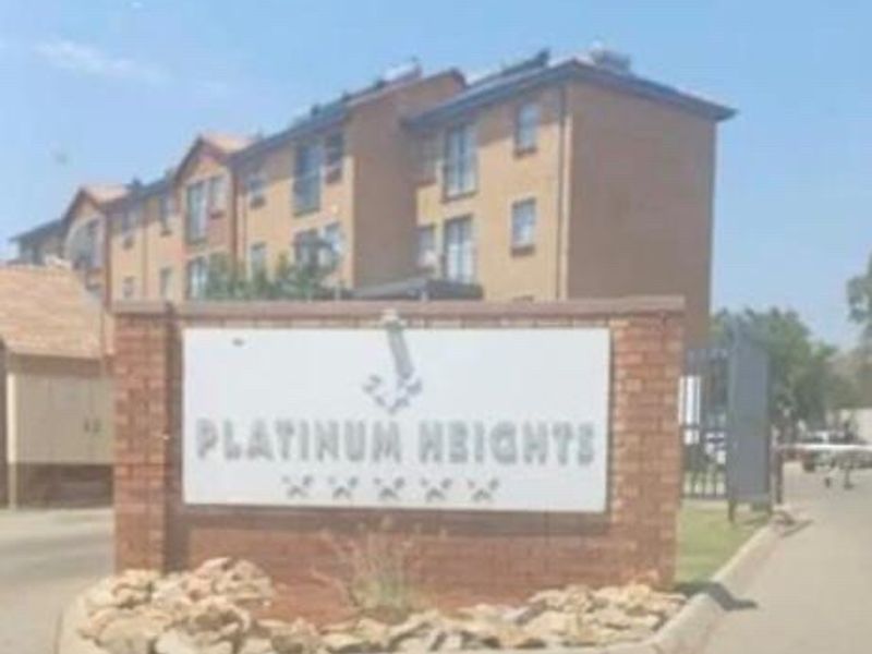 Street view of the Platinum Heights apartment complex entrance, featuring a brick boundary wall and signage with the multi-story residential building in the background.