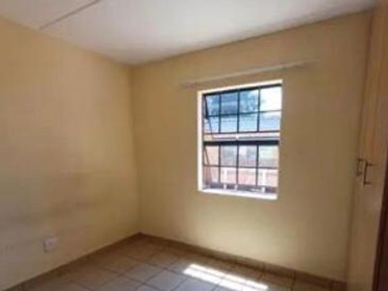 An empty bedroom featuring tiled flooring, built-in cupboards, and a window, requiring minor cosmetic updates to the wall finishes.