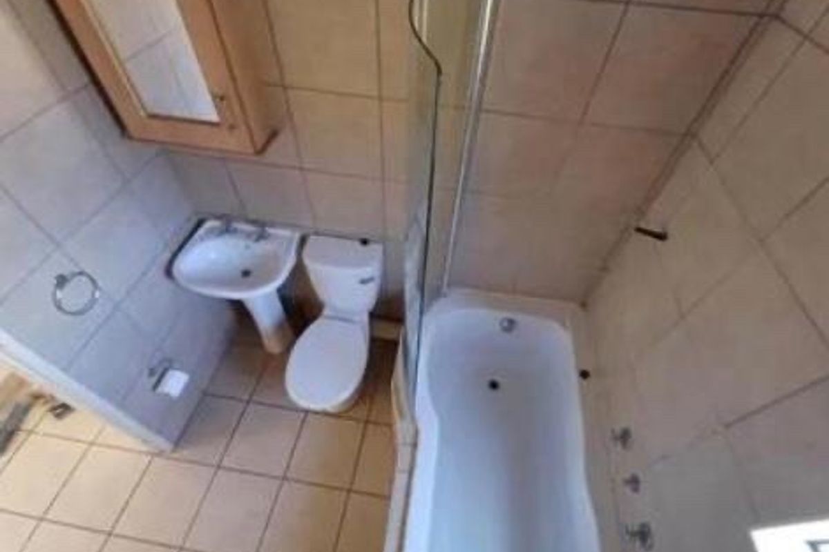 A functional bathroom featuring a pedestal basin, toilet, and a bathtub with a glass shower screen, finished with neutral wall and floor tiling.