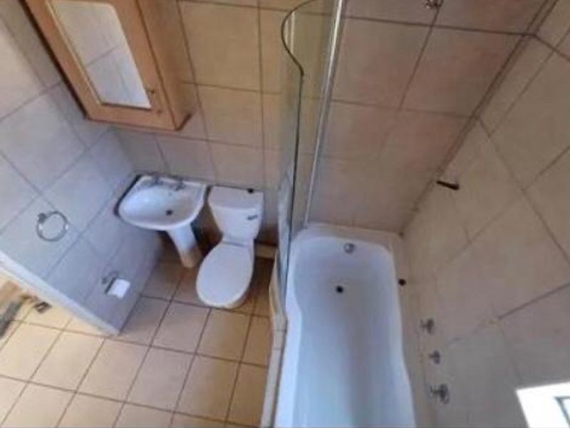 A functional bathroom featuring a pedestal basin, toilet, and a bathtub with a glass shower screen, finished with neutral wall and floor tiling.