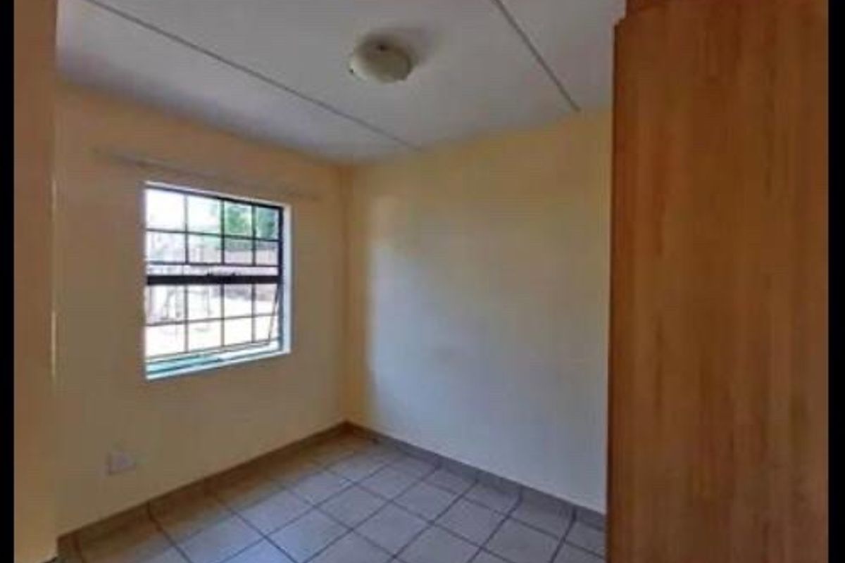 A simple, empty bedroom featuring tiled flooring, a built-in cupboard, and a window with security bars.