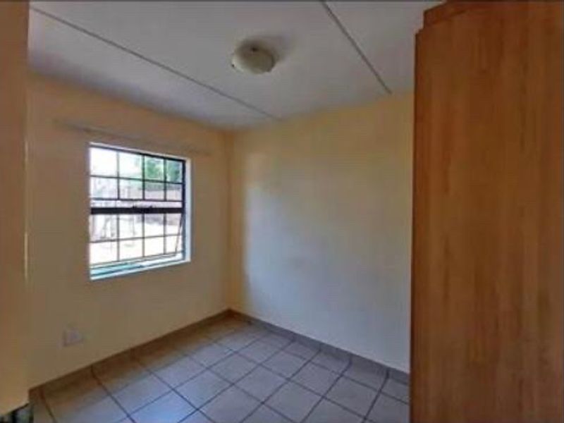 A simple, empty bedroom featuring tiled flooring, a built-in cupboard, and a window with security bars.