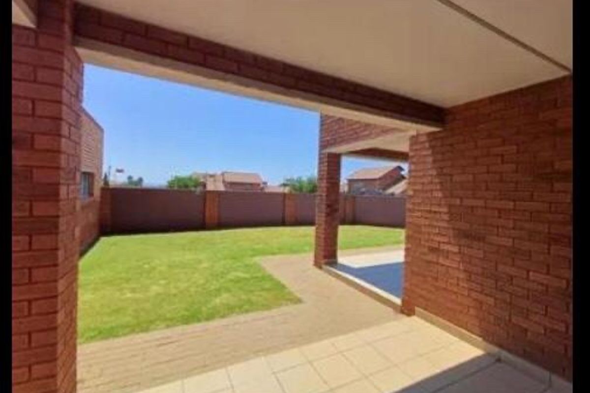 A covered patio area featuring exposed brick pillars and tiled flooring, overlooking a private garden with a paved walkway and perimeter wall.