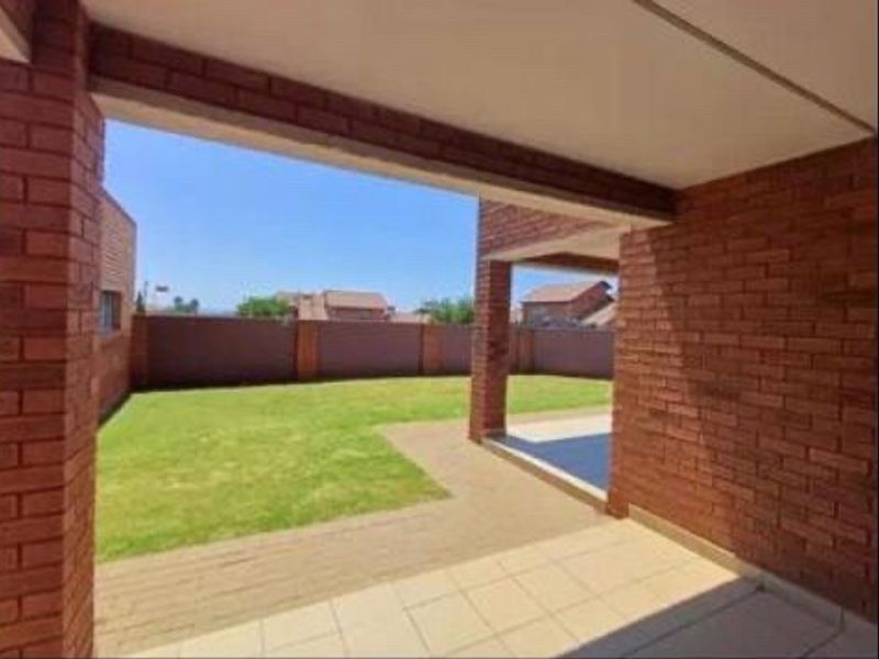 A covered patio area featuring exposed brick pillars and tiled flooring, overlooking a private garden with a paved walkway and perimeter wall.