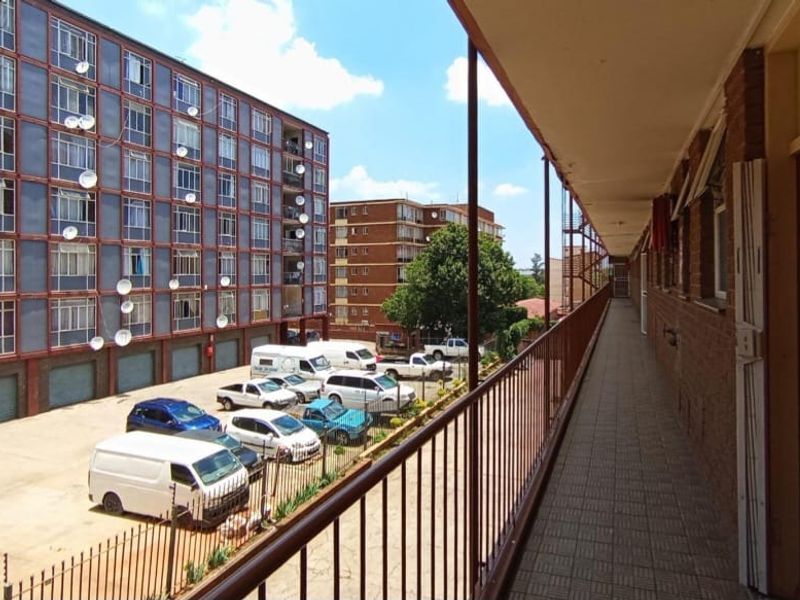 An exterior covered balcony walkway overlooking the apartment complex parking area and neighboring buildings.