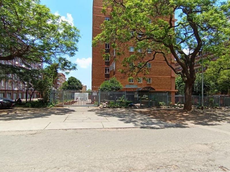 Exterior view of a multi-story brick apartment building featuring secure gated access, paved driveway, and mature landscaping.