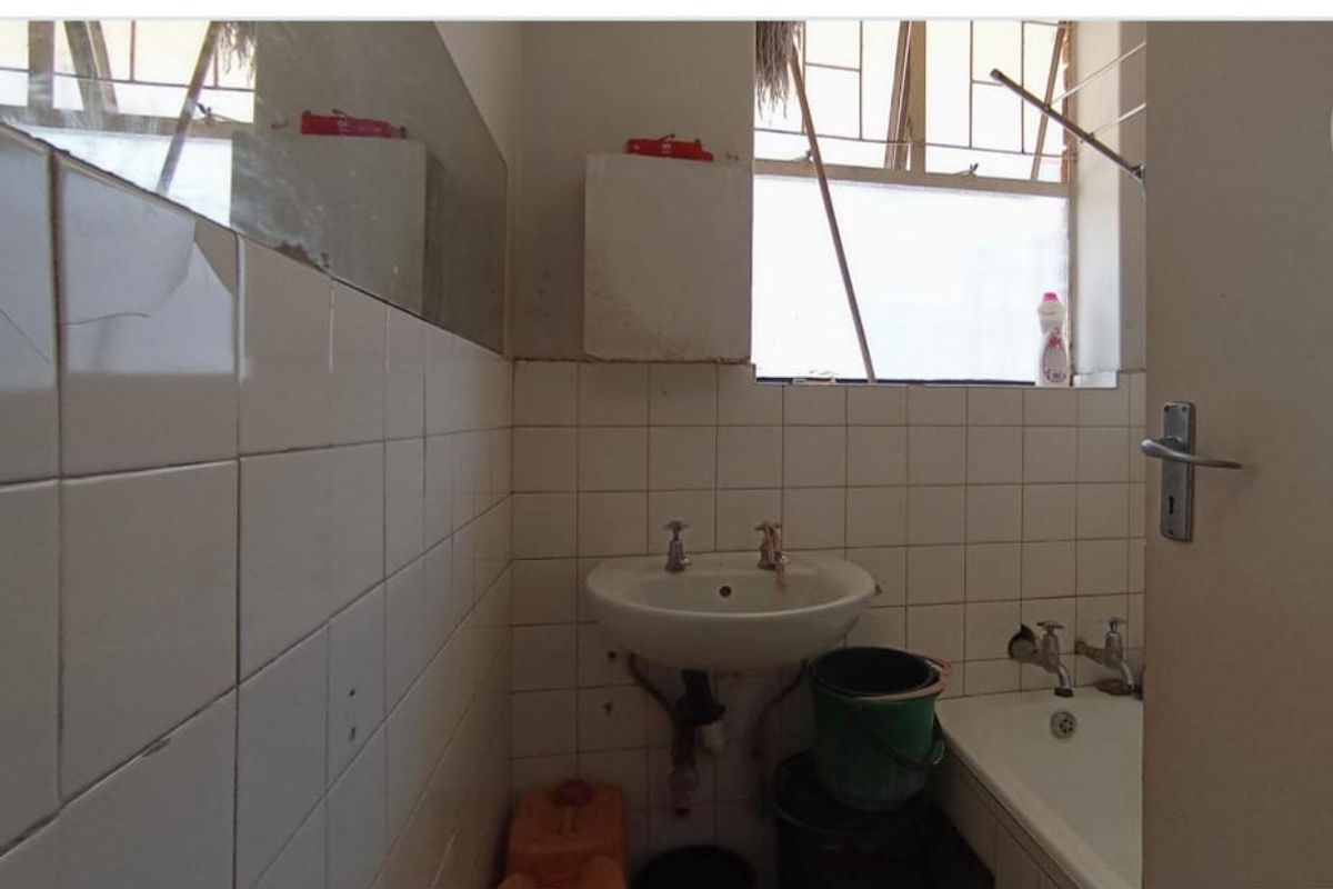 A dated bathroom featuring a pedestal basin, bathtub, and tiled walls, requiring renovation to update the worn fixtures and finishes.