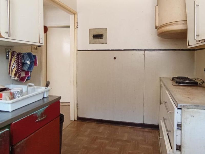 A dated kitchen featuring original cabinetry, laminate countertops, and an extractor fan, requiring cosmetic updates to modernize the space.