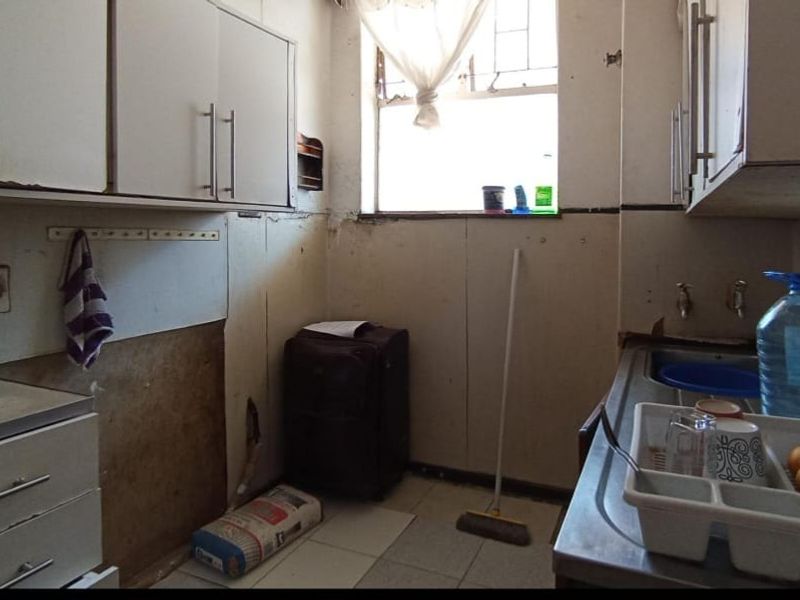 A dated kitchen area featuring built-in cabinetry and a stainless steel sink, requiring significant renovation and cosmetic updates to improve functionality and aesthetic appeal.