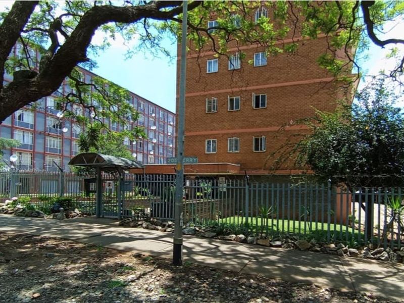 Street-level view of the apartment building facade featuring brick construction, secure perimeter fencing, and a gated pedestrian entrance.