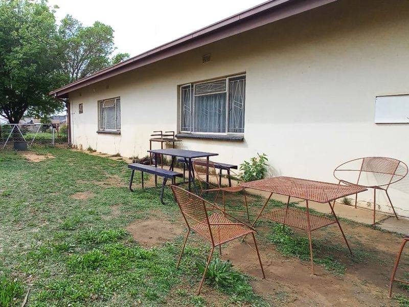 Rear exterior view of the house featuring a simple garden area with metal window frames and basic structural finishes.