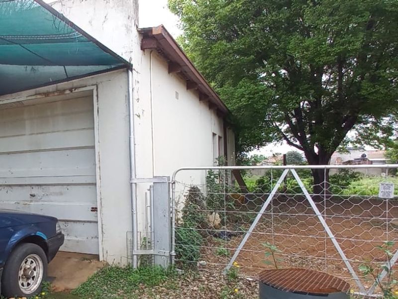 Exterior view of a single garage featuring a metal door, adjacent shade cloth carport, and perimeter wire fencing.
