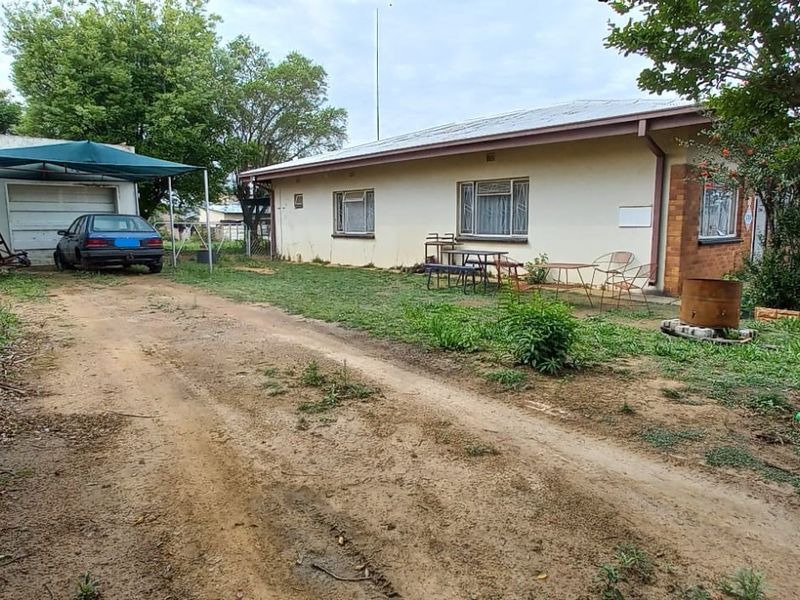 Rear view of the property featuring a single garage, carport, and a large garden area with a dirt driveway.