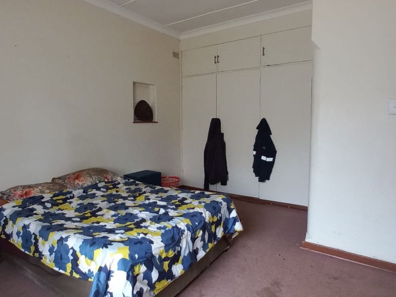 A bedroom featuring built-in cupboards, a wall niche, and carpet flooring. The space is functional but would benefit from cosmetic updates.