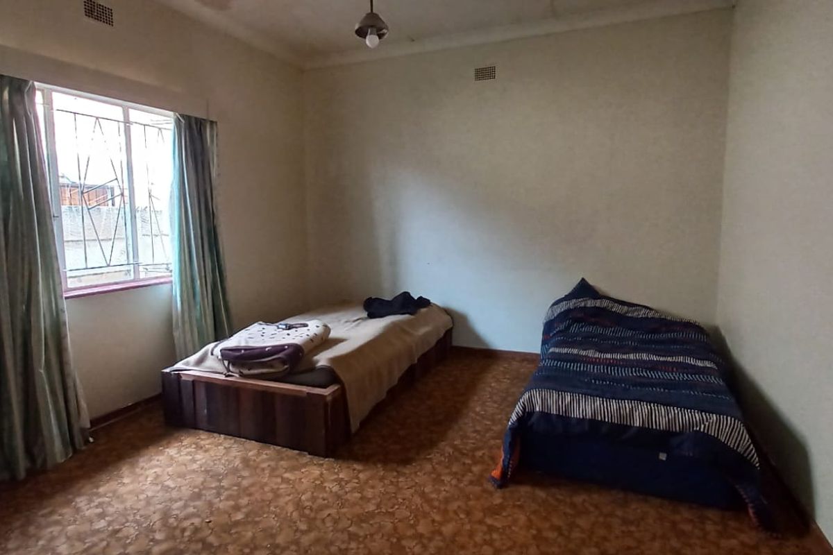 A bedroom featuring a window with security bars, coving, and dated flooring, offering a blank canvas for renovation and modernization.