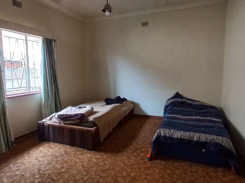 A bedroom featuring a window with security bars, coving, and dated flooring, offering a blank canvas for renovation and modernization.