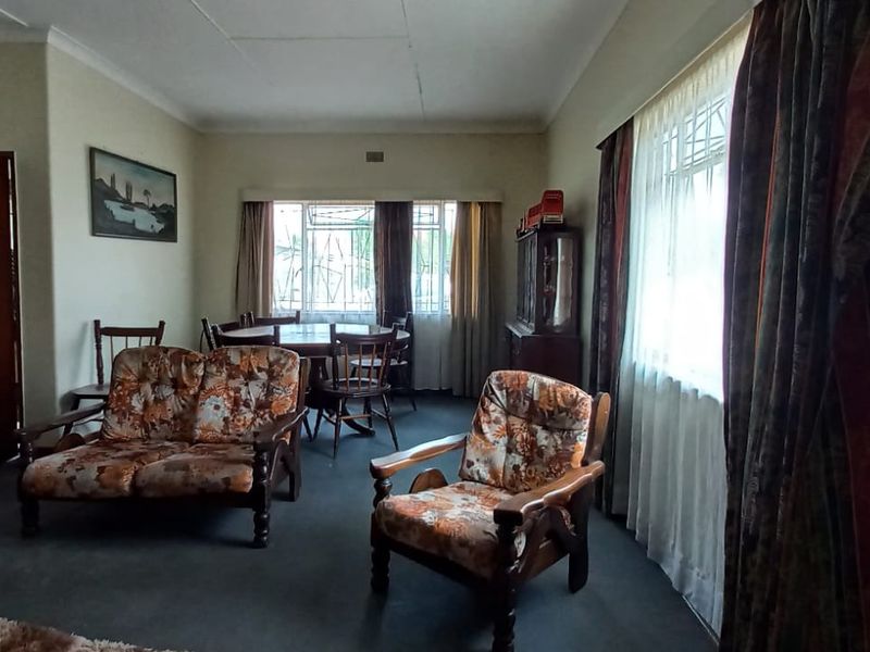 A spacious living room featuring neutral walls, carpeted flooring, and large windows with security bars, offering a functional and well-lit living space.